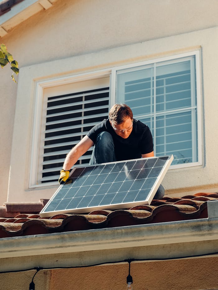 About A worker installing a solar panel on a residential rooftop under bright sunlight.